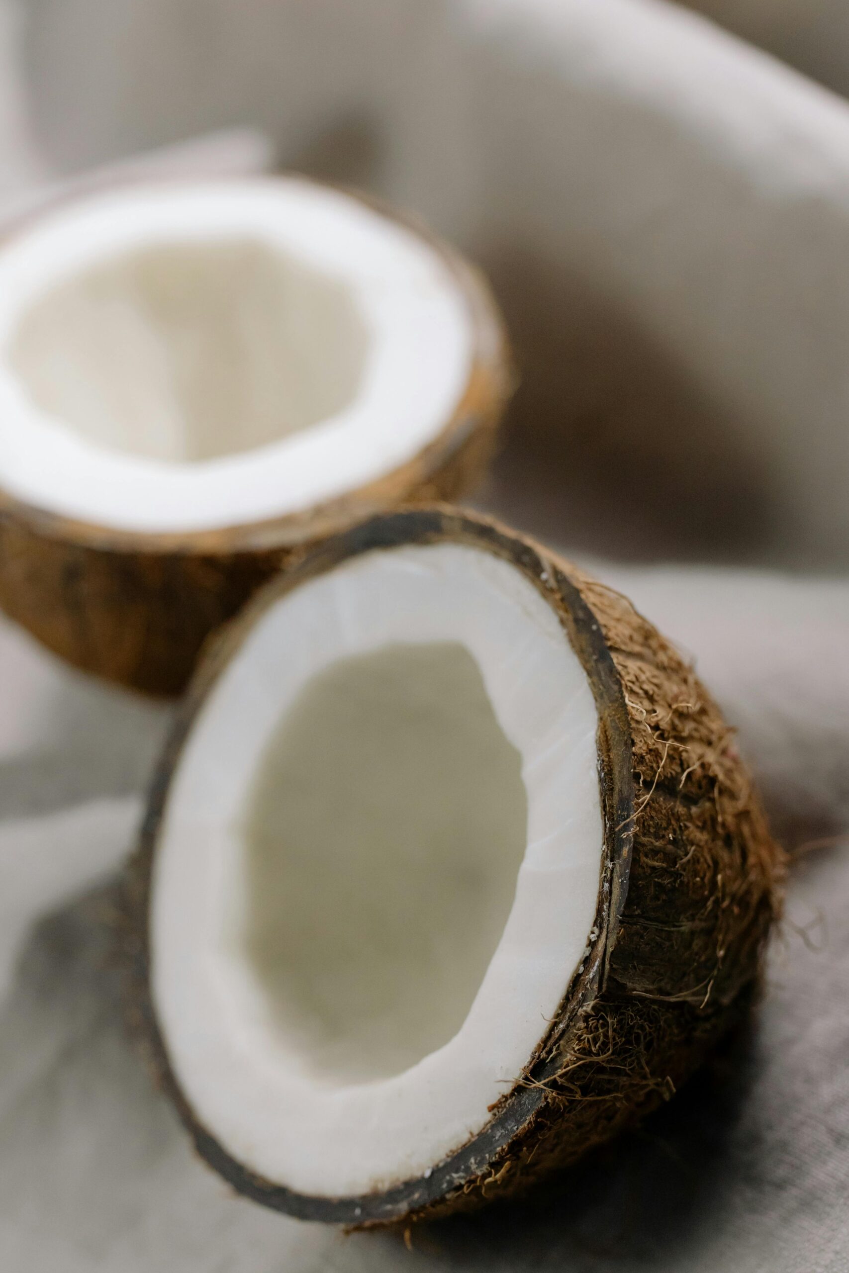Close-up of fresh, cracked coconut halves on a soft, textured background perfect for tropical themes.